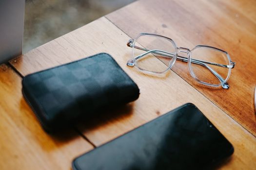 Stylish eyeglasses, wallet, and smartphone on a wooden table. Elegant composition.