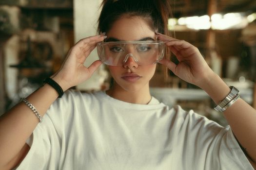 Young woman in casual fashion wearing safety glasses indoors.